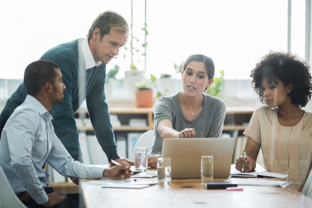 two men and two women working around a laptop
